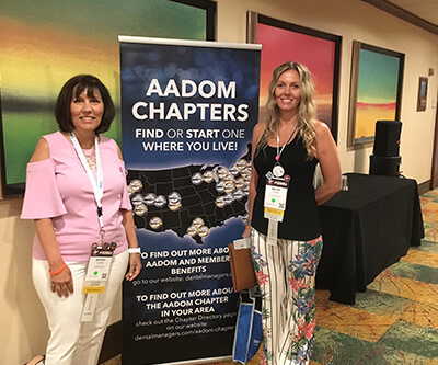 Two of our team standing either side of an AADOM Chapters sign