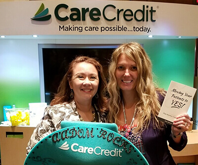 Two woman standing in front of a CareCredit logo and smiling